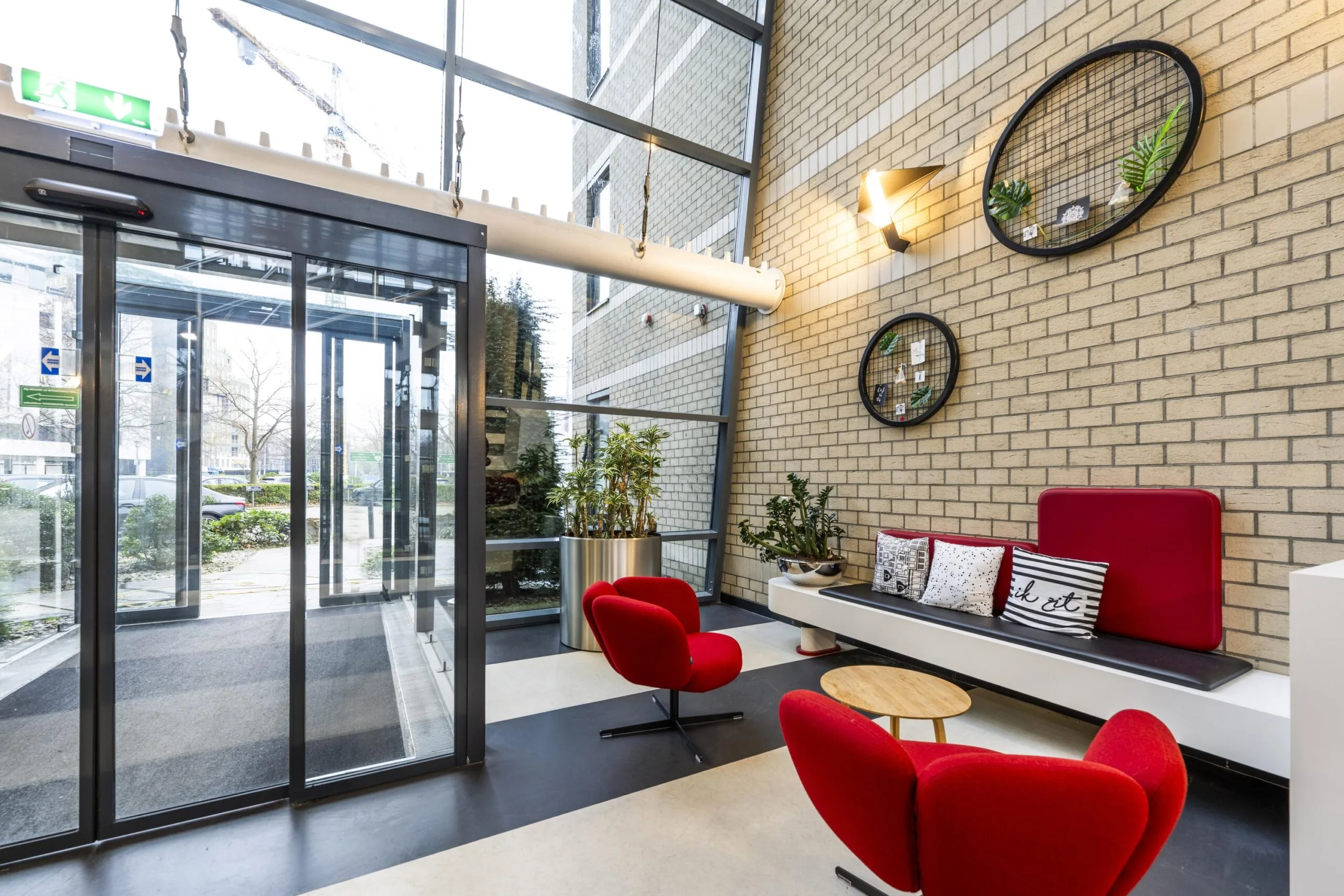 Een moderne entree met glazen schuifdeur, rode stoelen, en een bakstenen muur met decoratieve elementen.