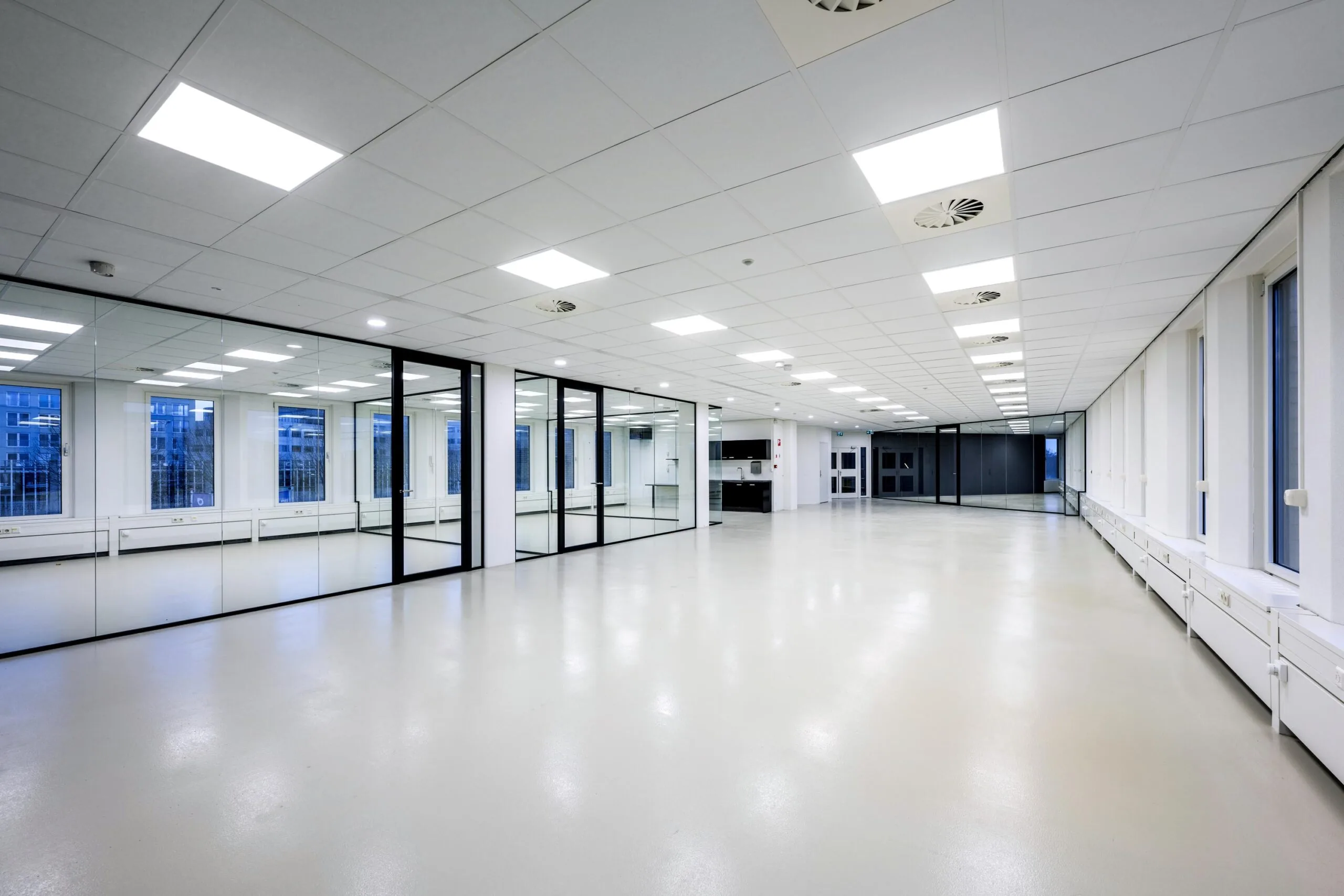 Een ruime, lege kantoorruimte met glazen wanden en een verlaagd systeemplafond aan de Neptunusstraat.