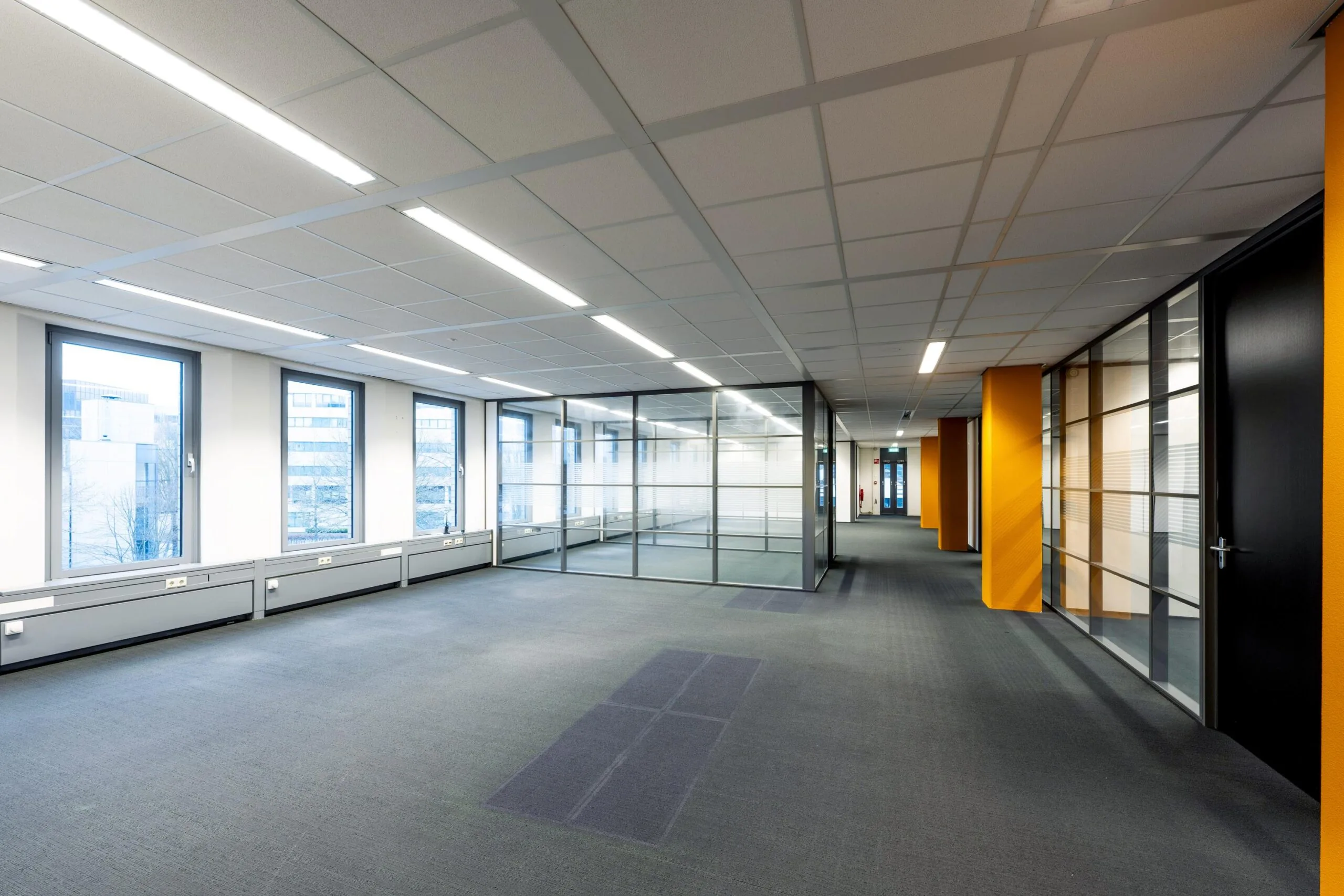 Een leeg, modern kantoorinterieur met grote ramen en glazen wanden aan de Neptunusstraat.