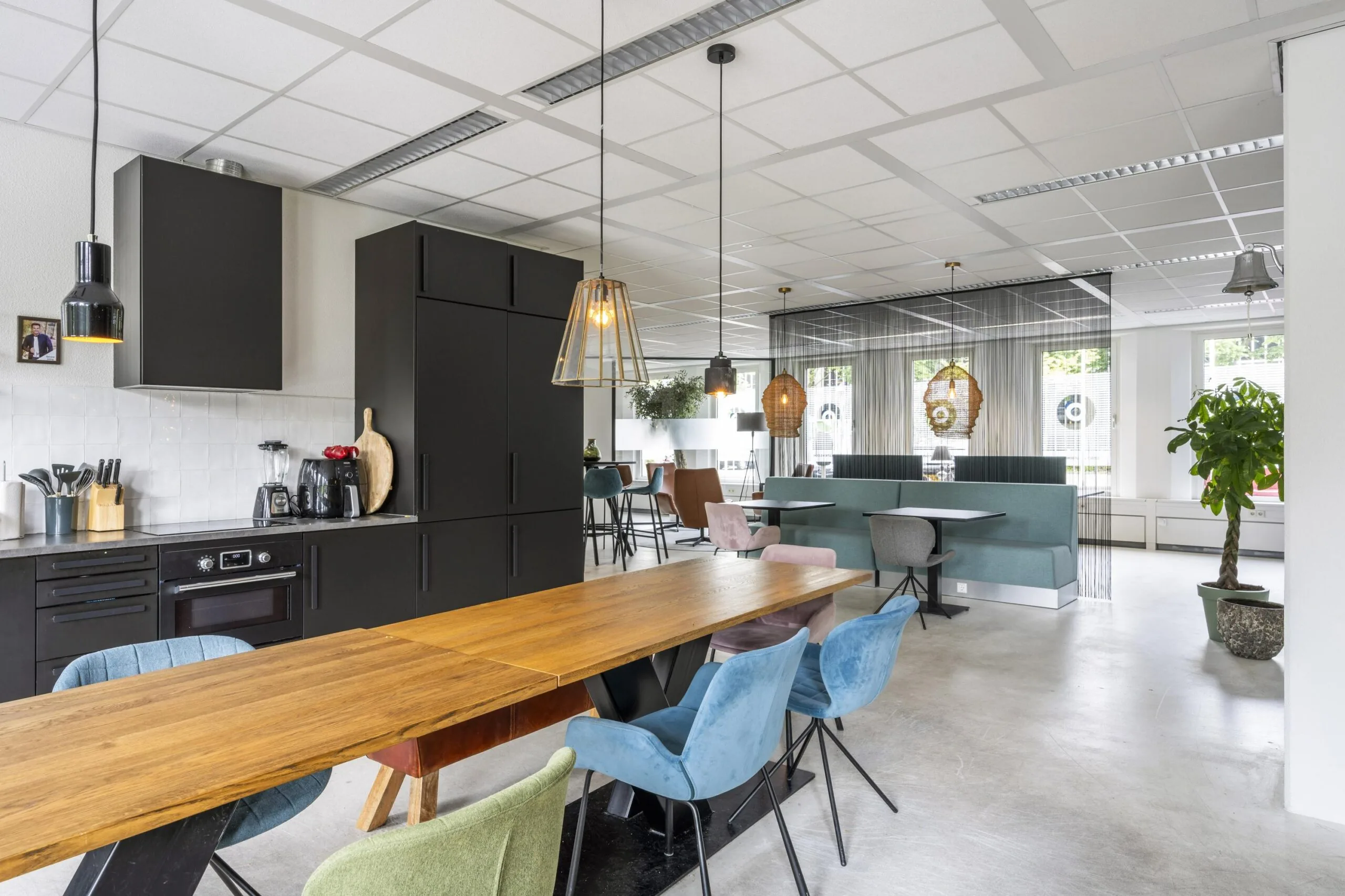 Moderne kantoor keuken met houten tafels, kleurrijke stoelen en planten.