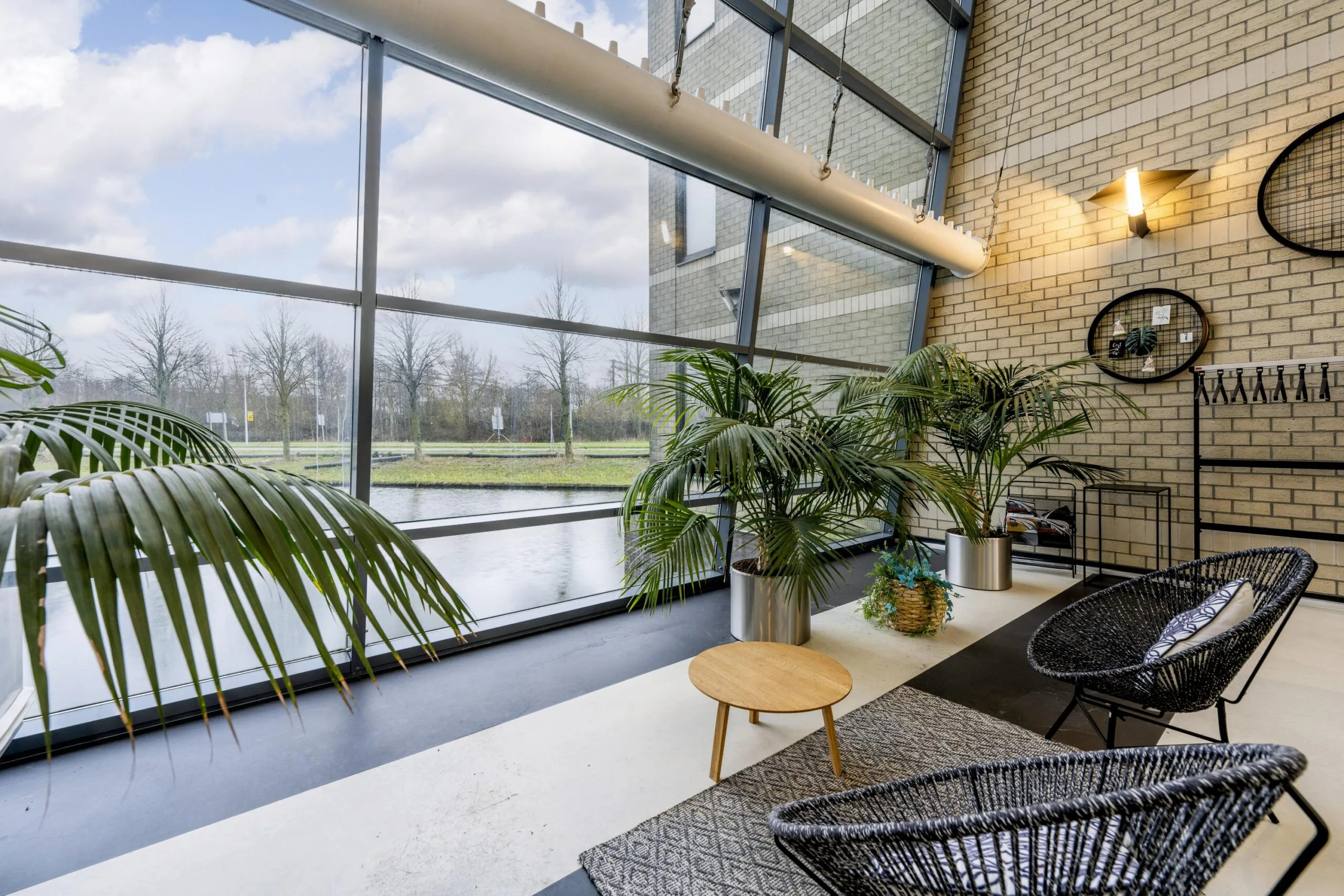 Een moderne lounge met grote ramen, veel planten en stijlvolle zitstoelen.
