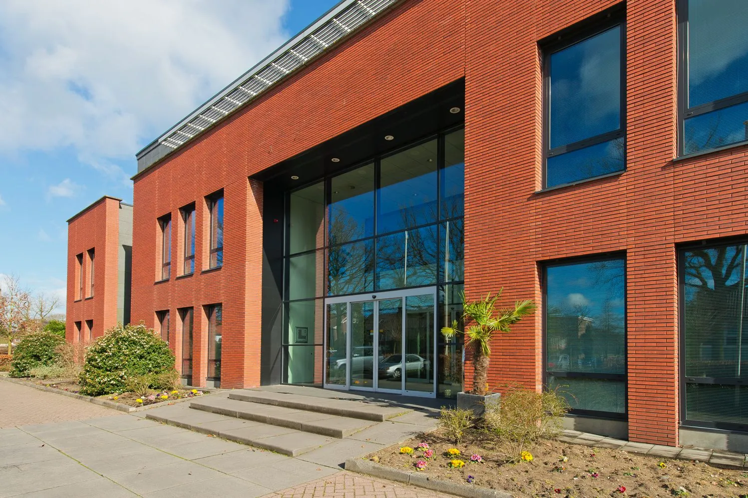 Vooraanzicht van een modern gebouw met rode bakstenen en grote glazen entree aan de Groenekanseweg.