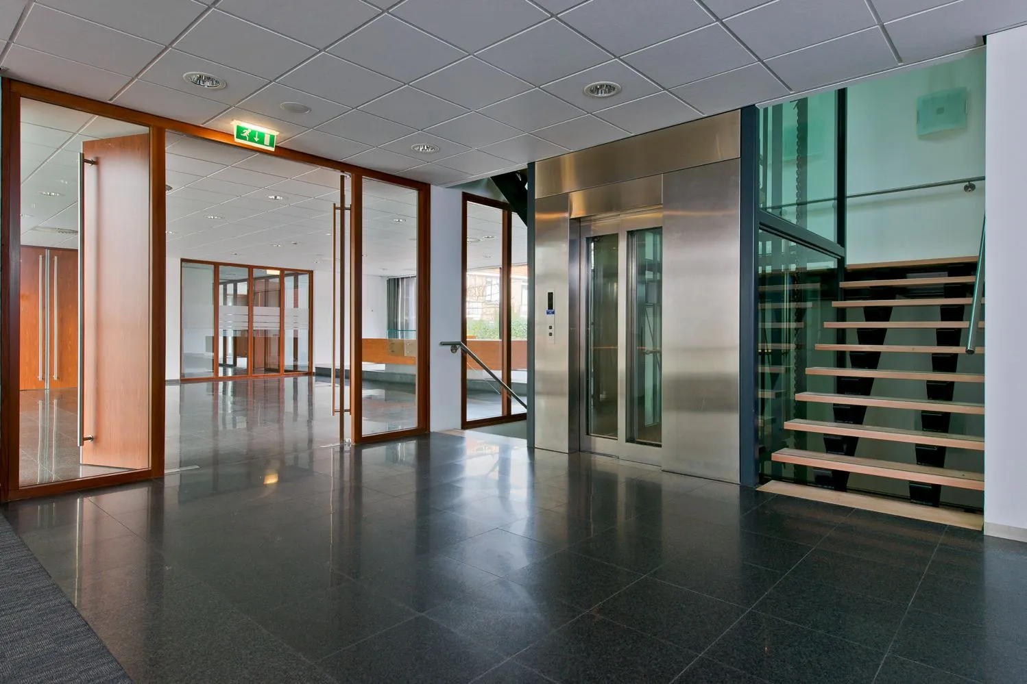 Een moderne gang met glazen deuren, een lift en een trap.