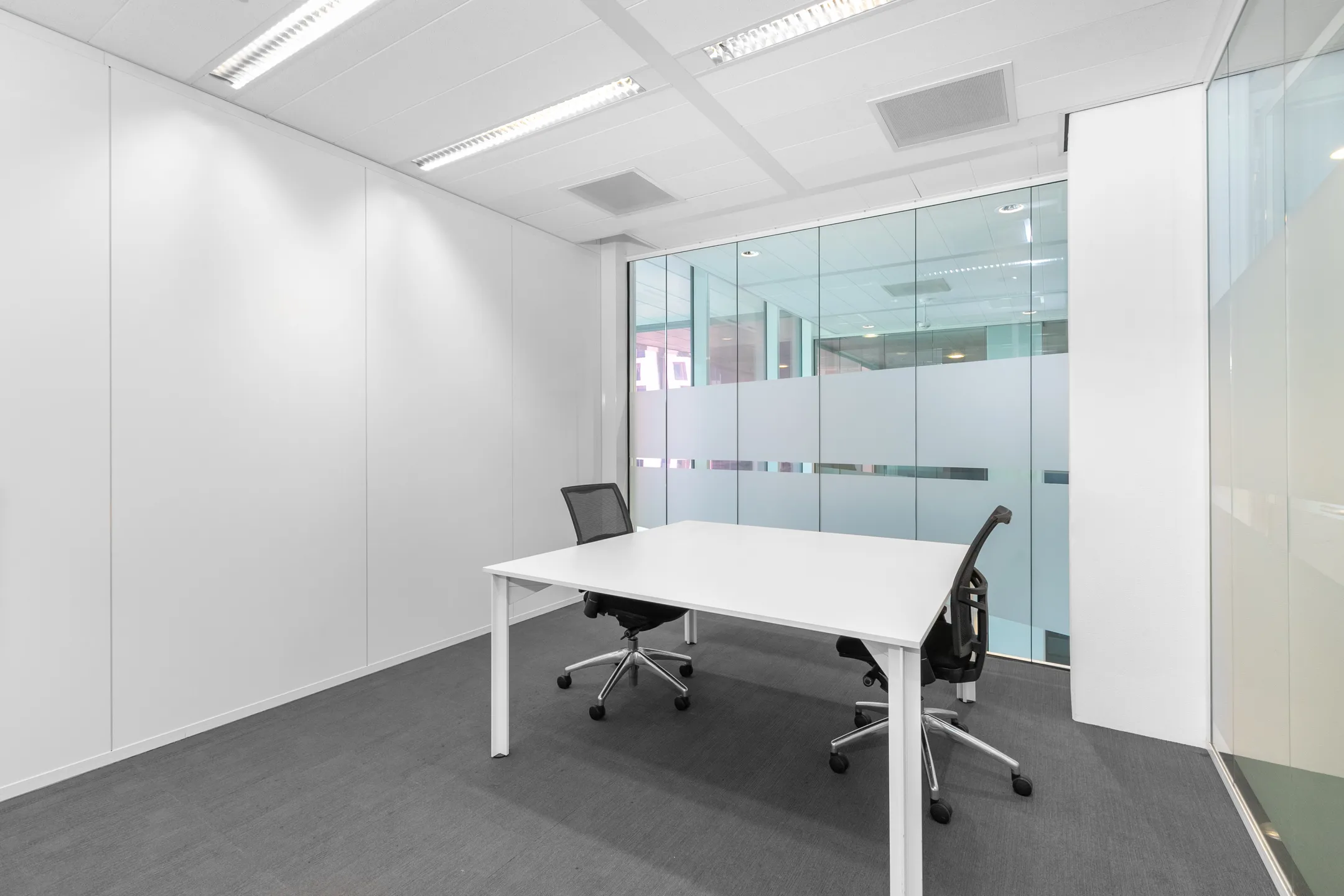 Een minimalistisch en modern ingerichte vergaderruimte met een witte tafel en twee zwarte kantoorstoelen.