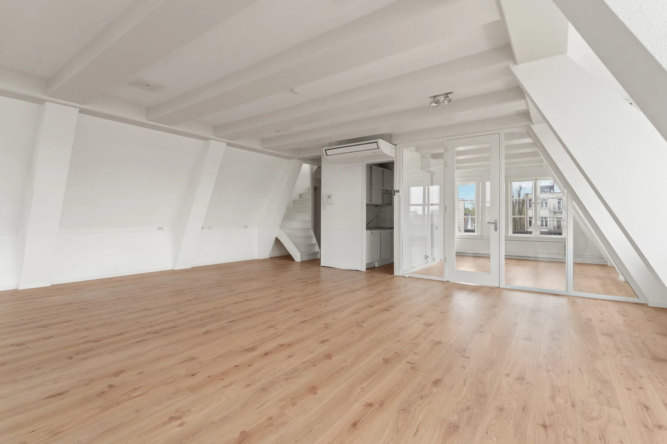 Een ruime, moderne zolderkamer met houten vloer en veel natuurlijke lichtinval.