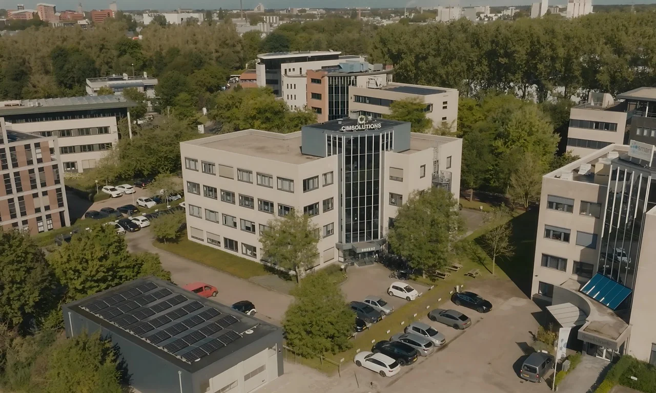 Luchtfoto van het kantoorgebouw van CIM Solutions omringd door bomen en geparkeerde auto's.