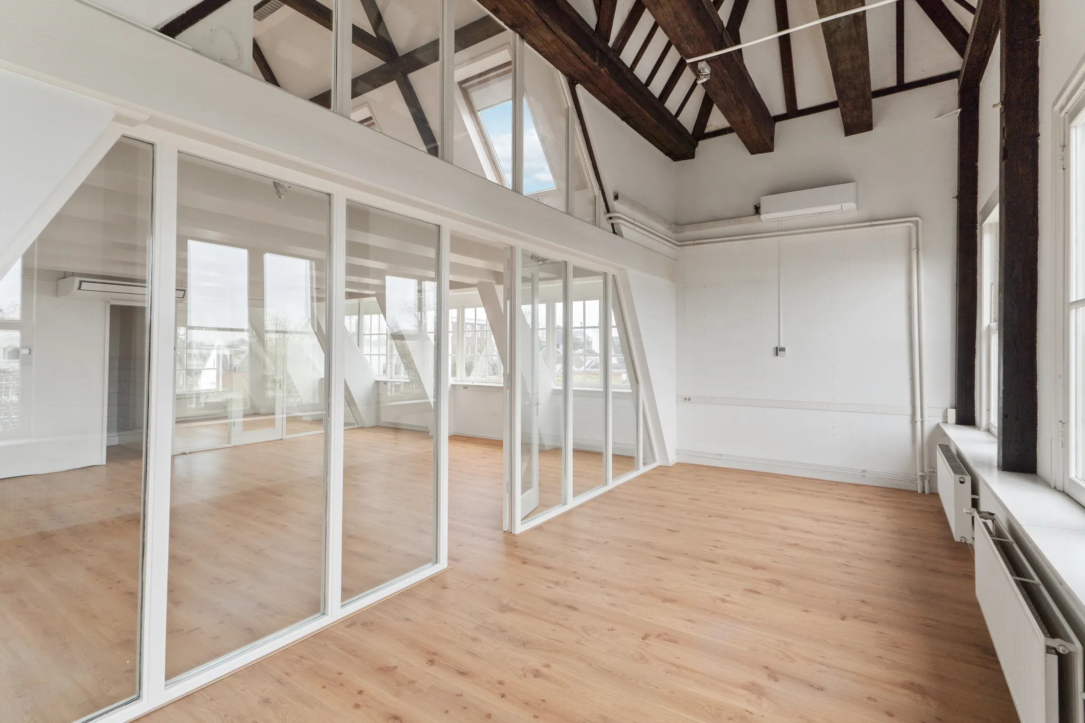 Een lichte en ruime kamer met houten vloeren en grote glazen wanden.