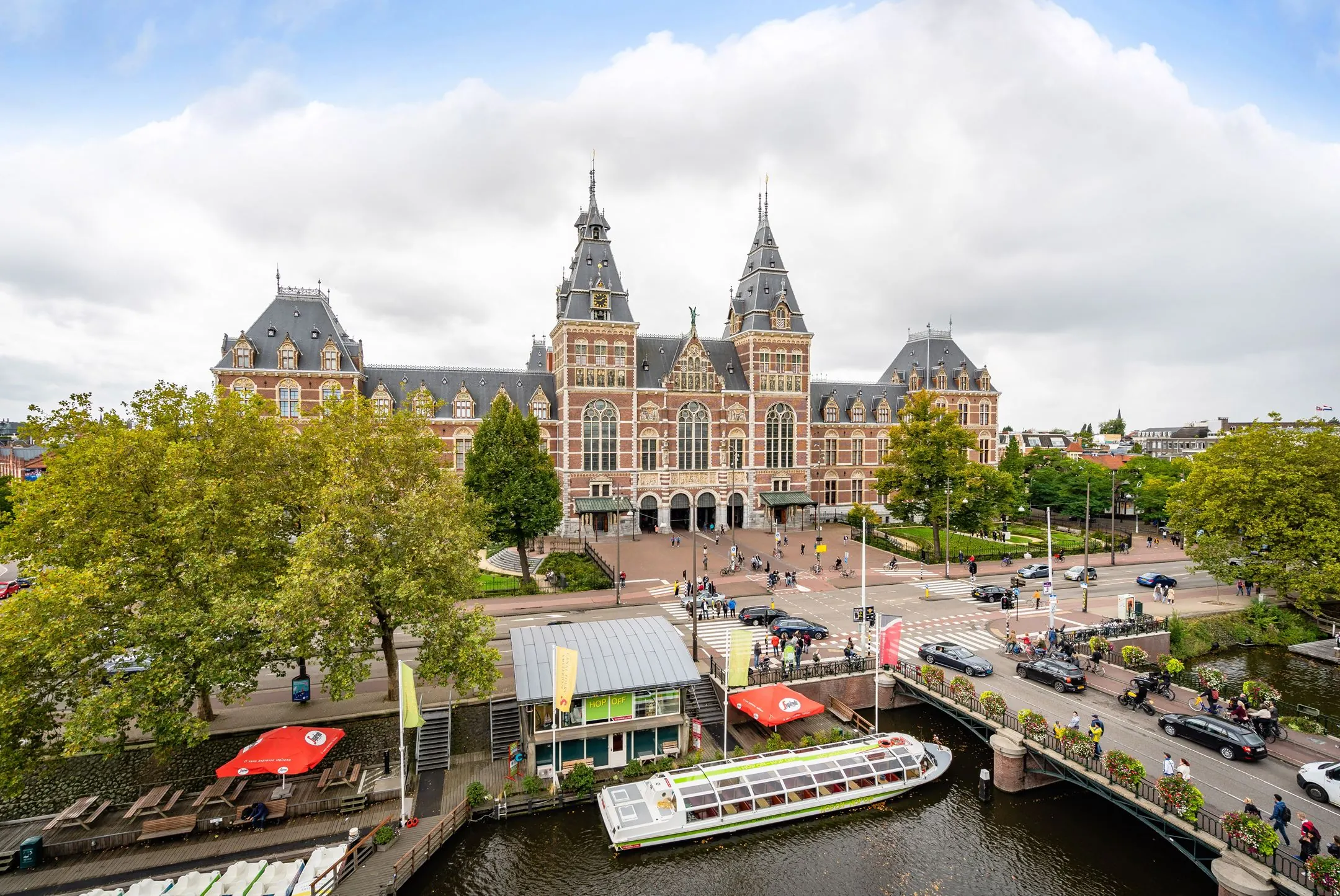 Voorgevel van het Rijksmuseum in Amsterdam met een rondvaartboot op de gracht op de voorgrond.