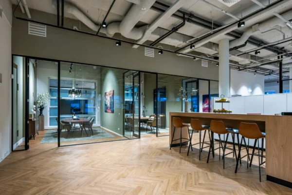 Een moderne kantoorruimte met glazen wanden, een grote vergadertafel en een hoge houten tafel met barkrukken.