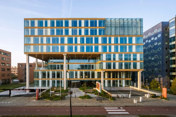 Modern kantoorgebouw met glazen gevel en gele accenten, gefotografeerd vanaf de straatkant.