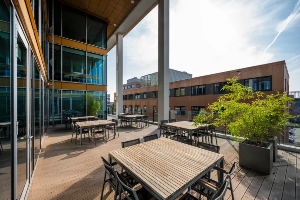 Zonnig dakterras met houten tafels, stoelen en groene planten bij kantoorgebouw 366_2160.