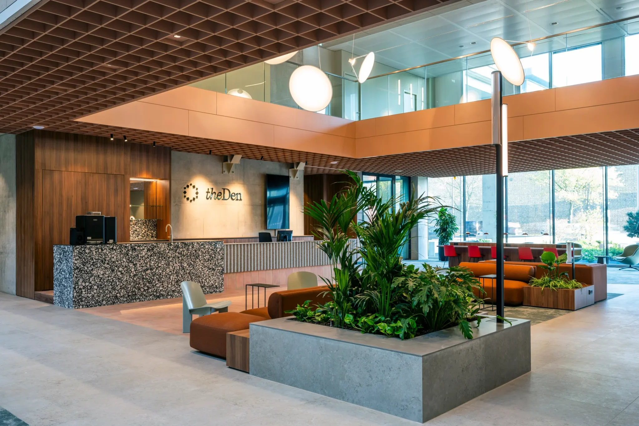 Moderne hotellobby van The Den met groene planten, zitgedeelte en een stijlvolle receptiebalie.
