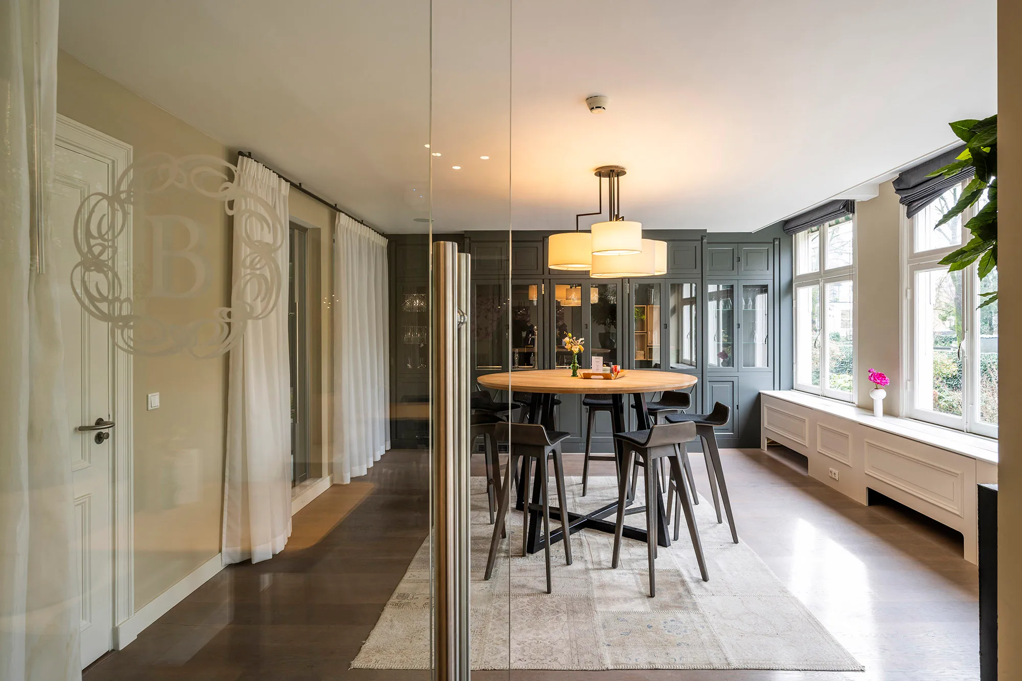 Een moderne eetkamer met een ronde houten tafel, hoge stoelen, en veel natuurlijk licht.