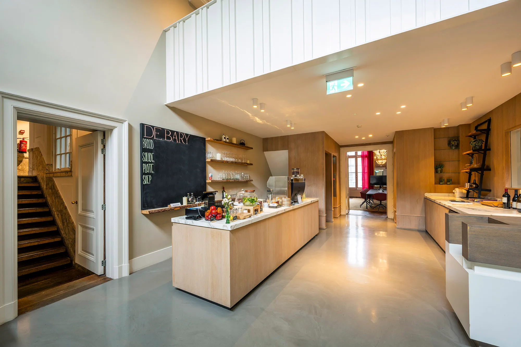Een moderne keuken met een balie, keukenplanken, en een krijtbord met het menu "De Bary".