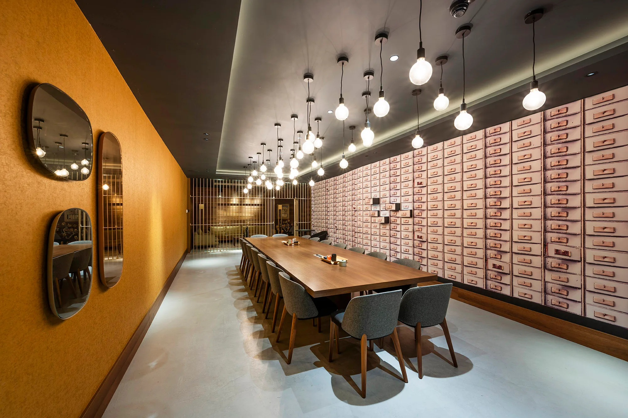 Een moderne vergaderruimte met een lange houten tafel en designverlichting tegen een muur met een patroon van ladefronten.