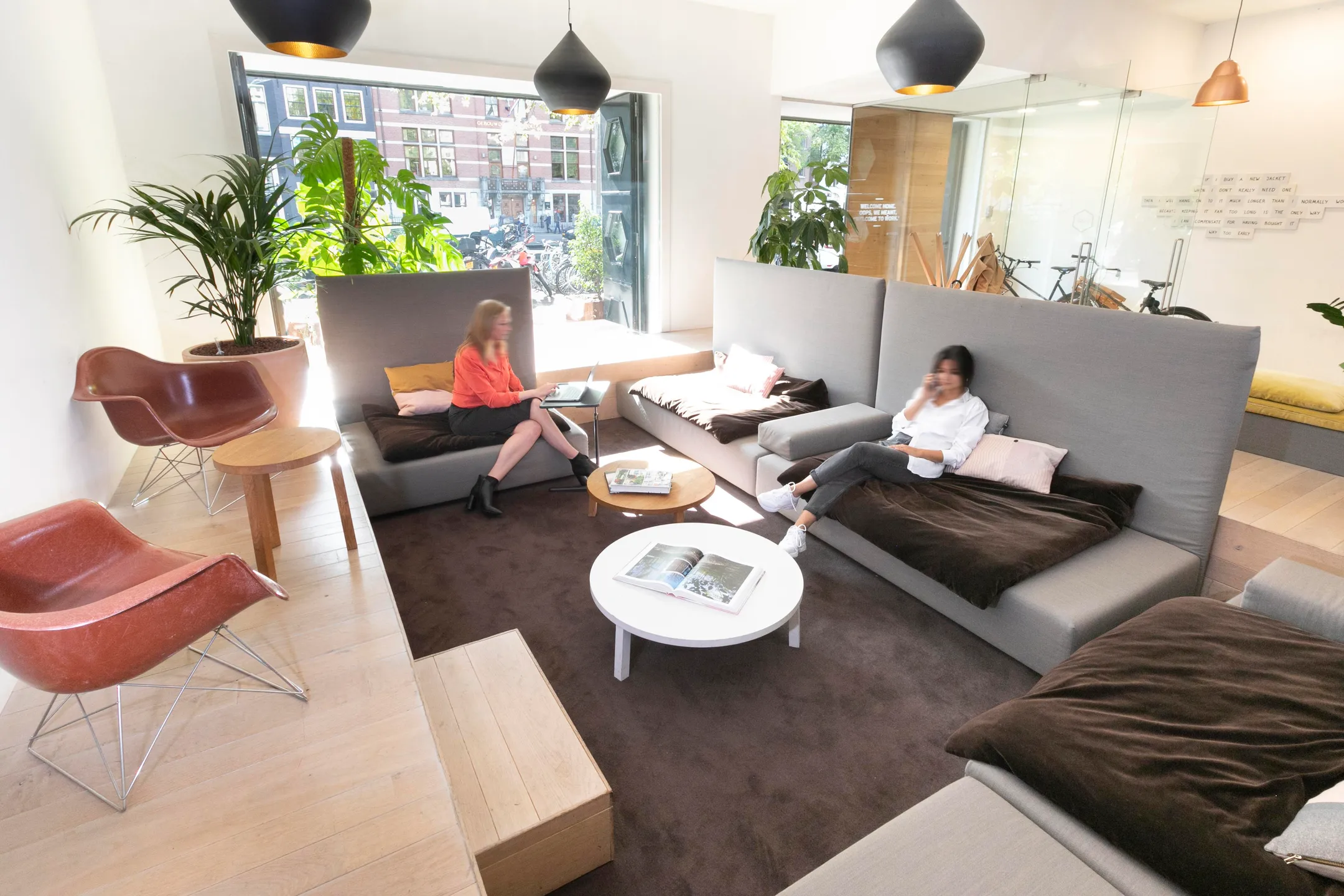 Twee mensen zitten in een moderne en lichte kantoorruimte met planten en comfortabele banken.