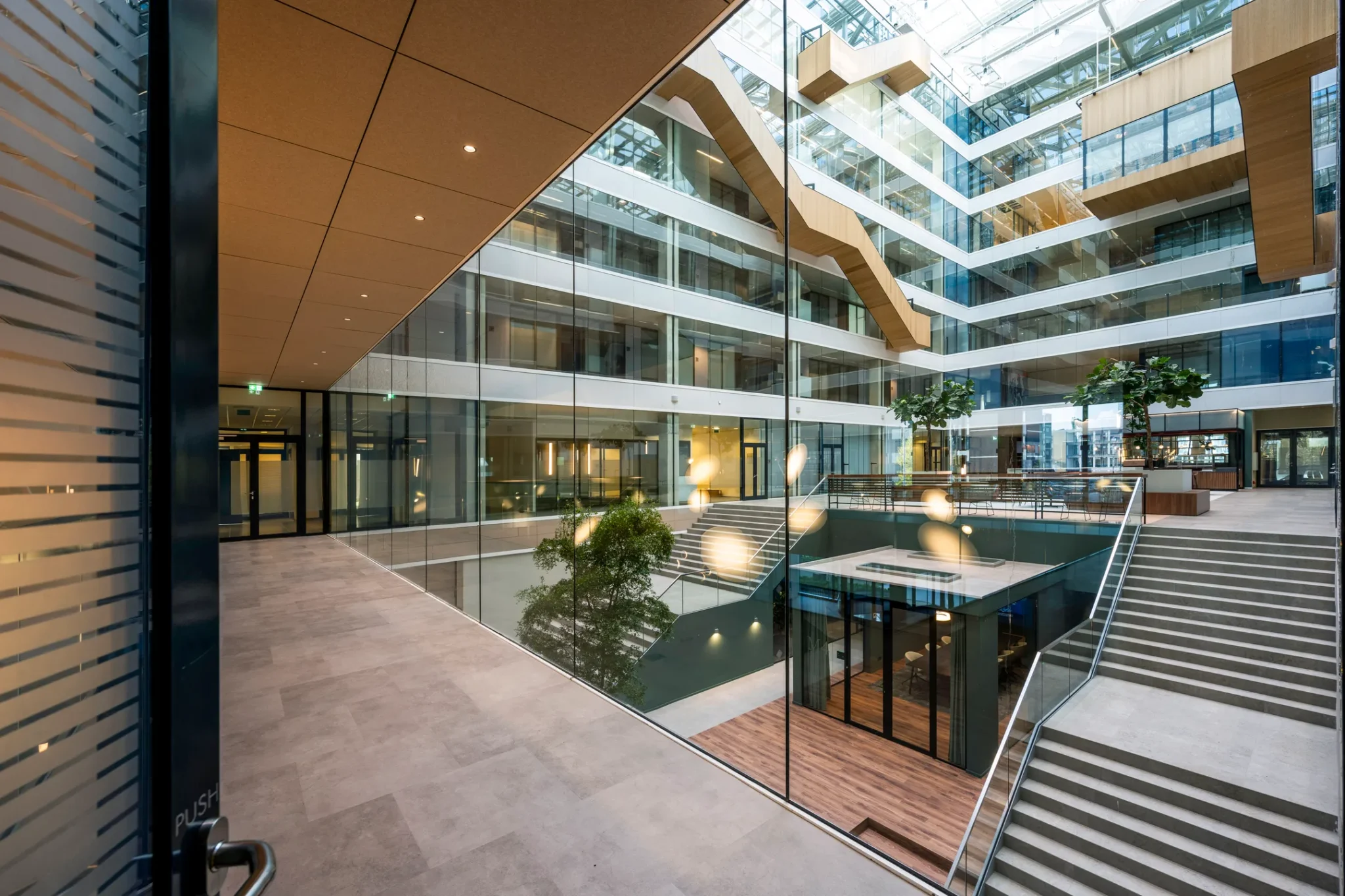 Moderne, ruimtelijke kantoorlobby met glazen wanden, houten accenten en meerdere verdiepingen.