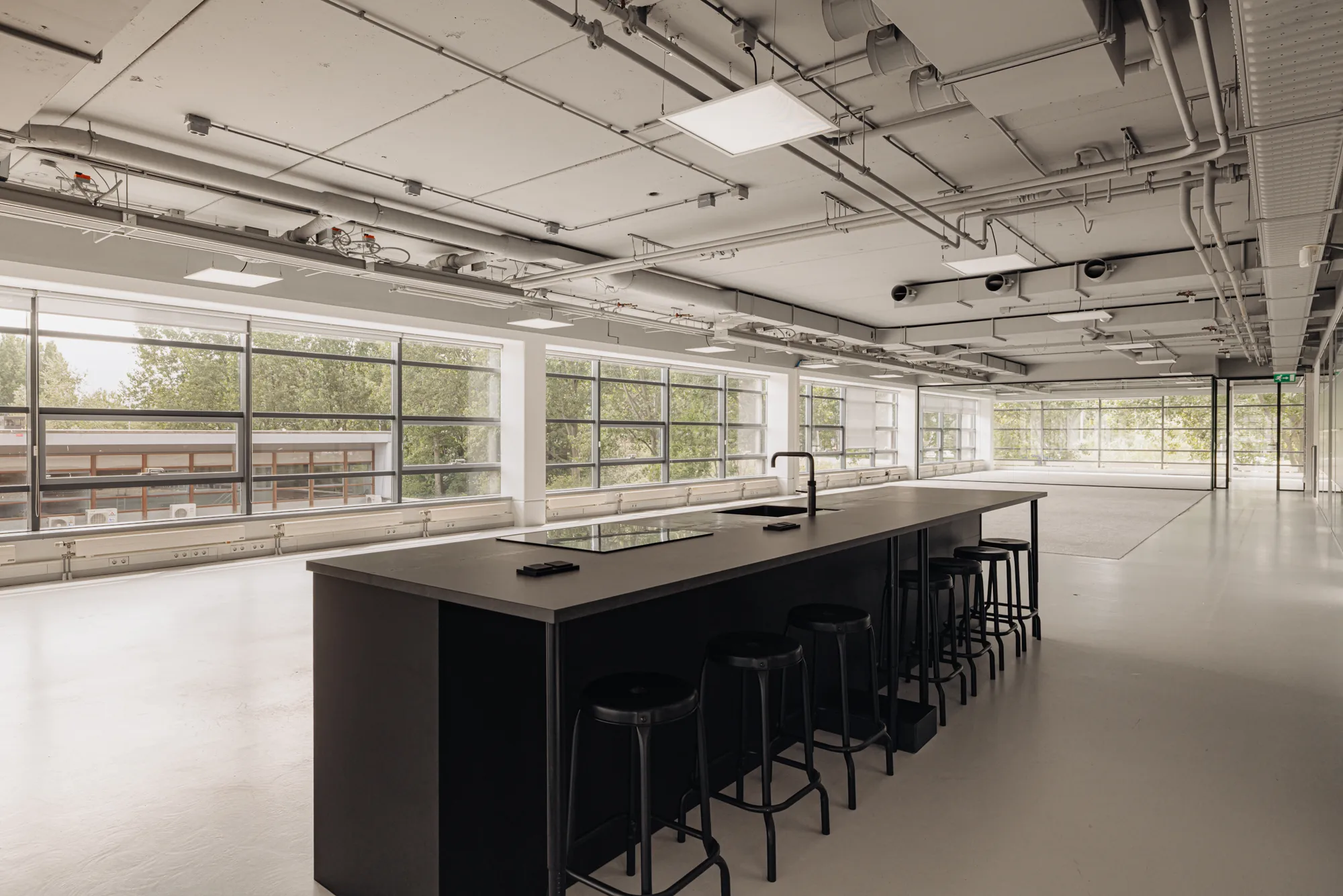 Een grote, open ruimte met een modern keukenblok en hoge ramen.
