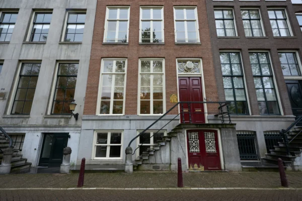 Gevel van een traditioneel Nederlands grachtenpand met een trap en rode voordeur.