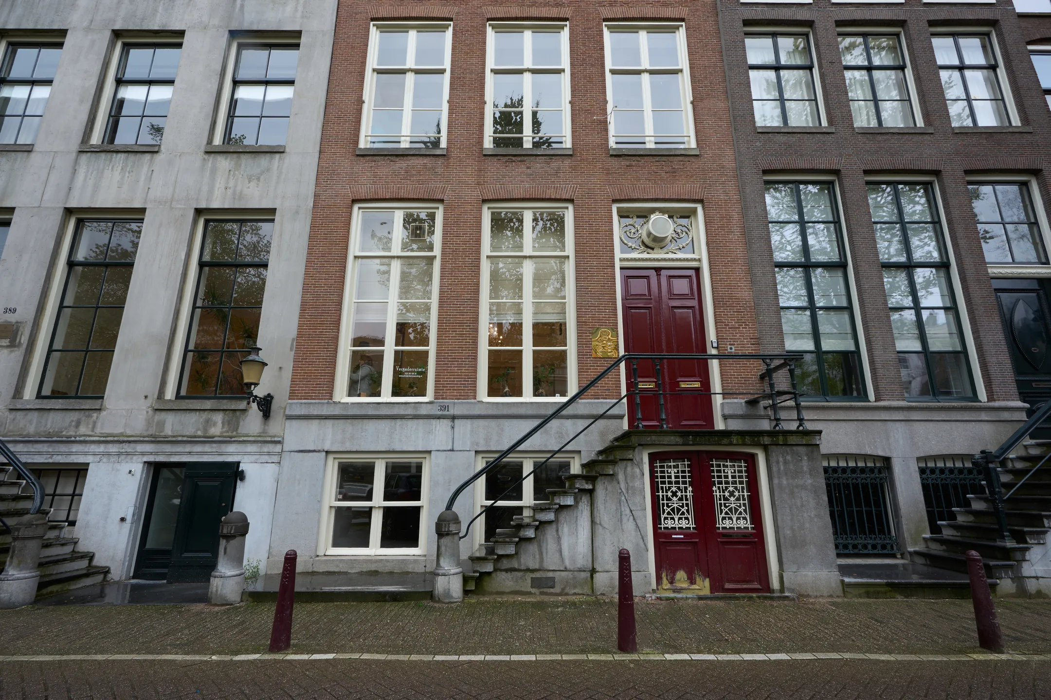 Gevel van een traditioneel Nederlands grachtenpand met een trap en rode voordeur.