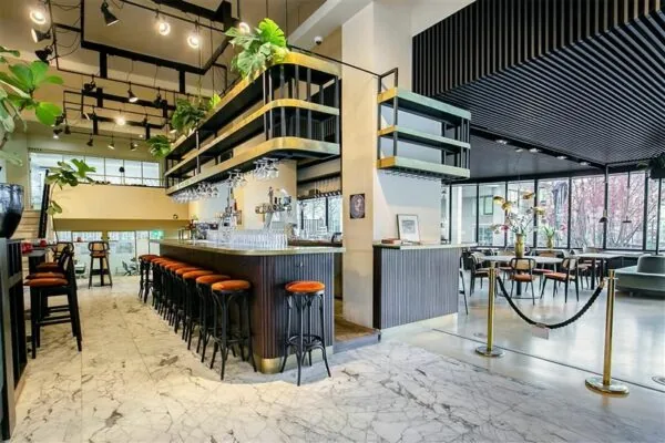 Moderne, stijlvol ingerichte bar met marmeren vloer, hoge barkrukken en veel natuurlijke lichtinval.