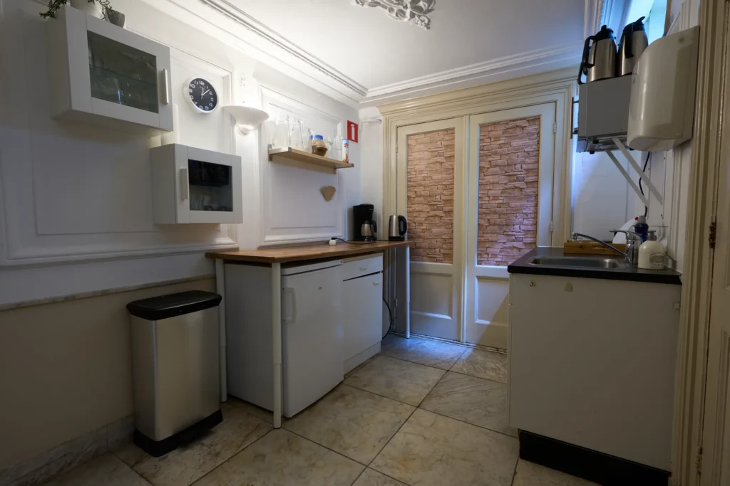 Een kleine keuken met witte kasten, gootsteen, glasplank en elektrische apparaten.