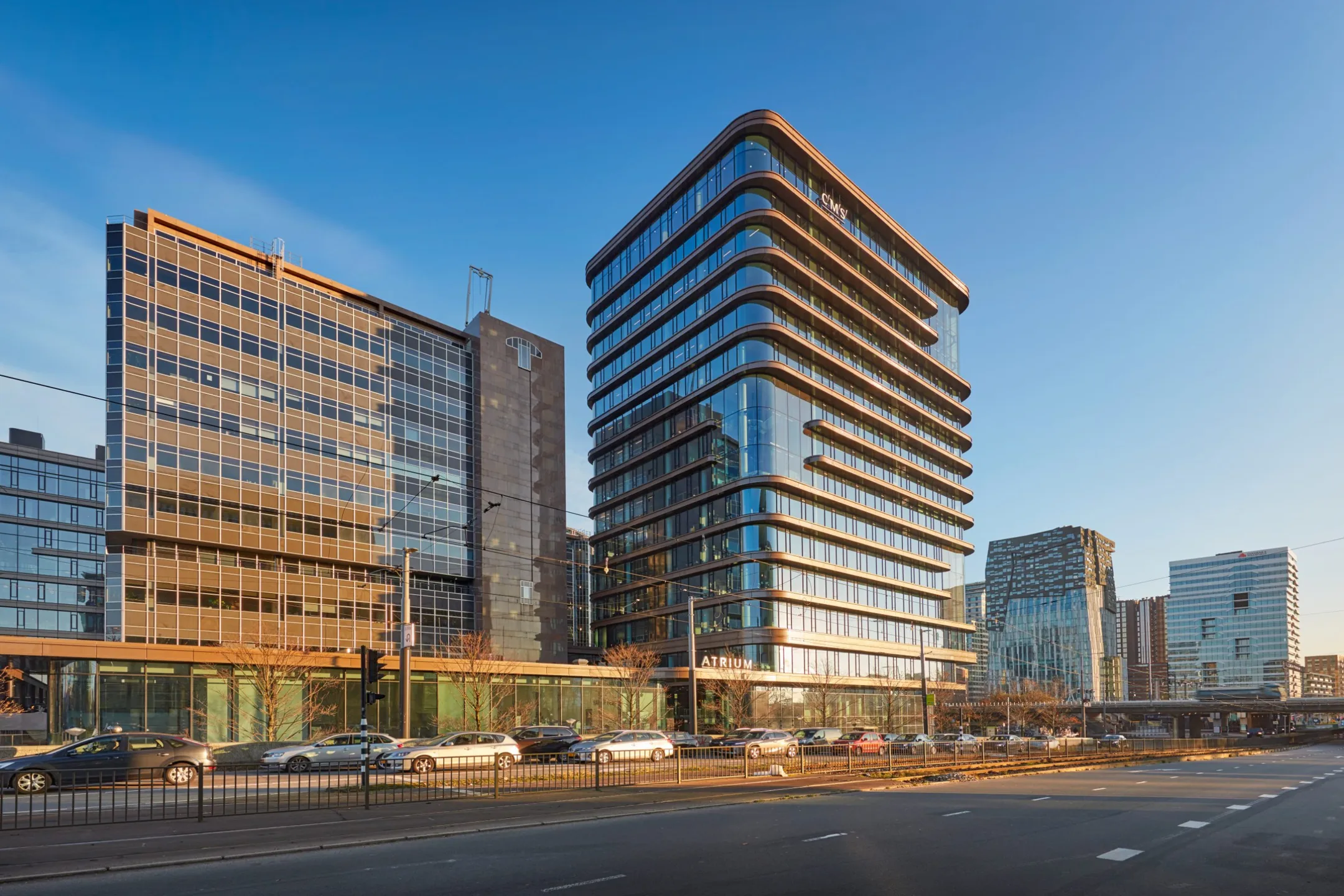 Moderne kantoorgebouwen langs een drukke weg bij ondergaande zon.
