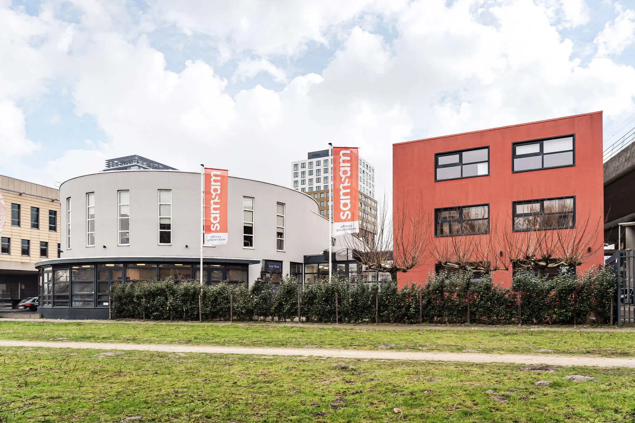 Een modern kantoorgebouw met een rode en witte gevel en "samsam" vlaggen aan de buitenkant.