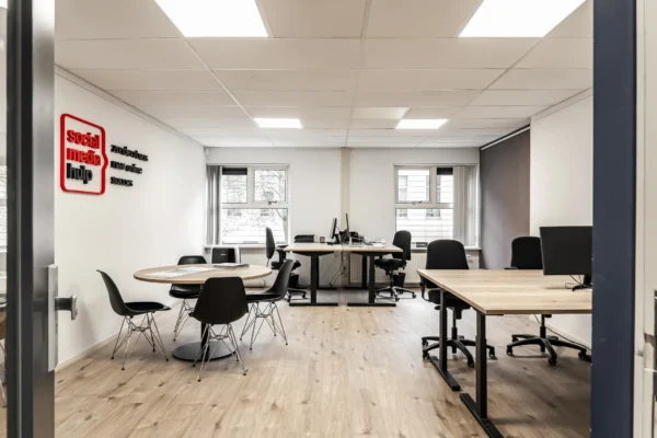 Een moderne kantoorruimte met bureaus, stoelen en een ronde tafel, met op de muur de woorden "social media hulp".