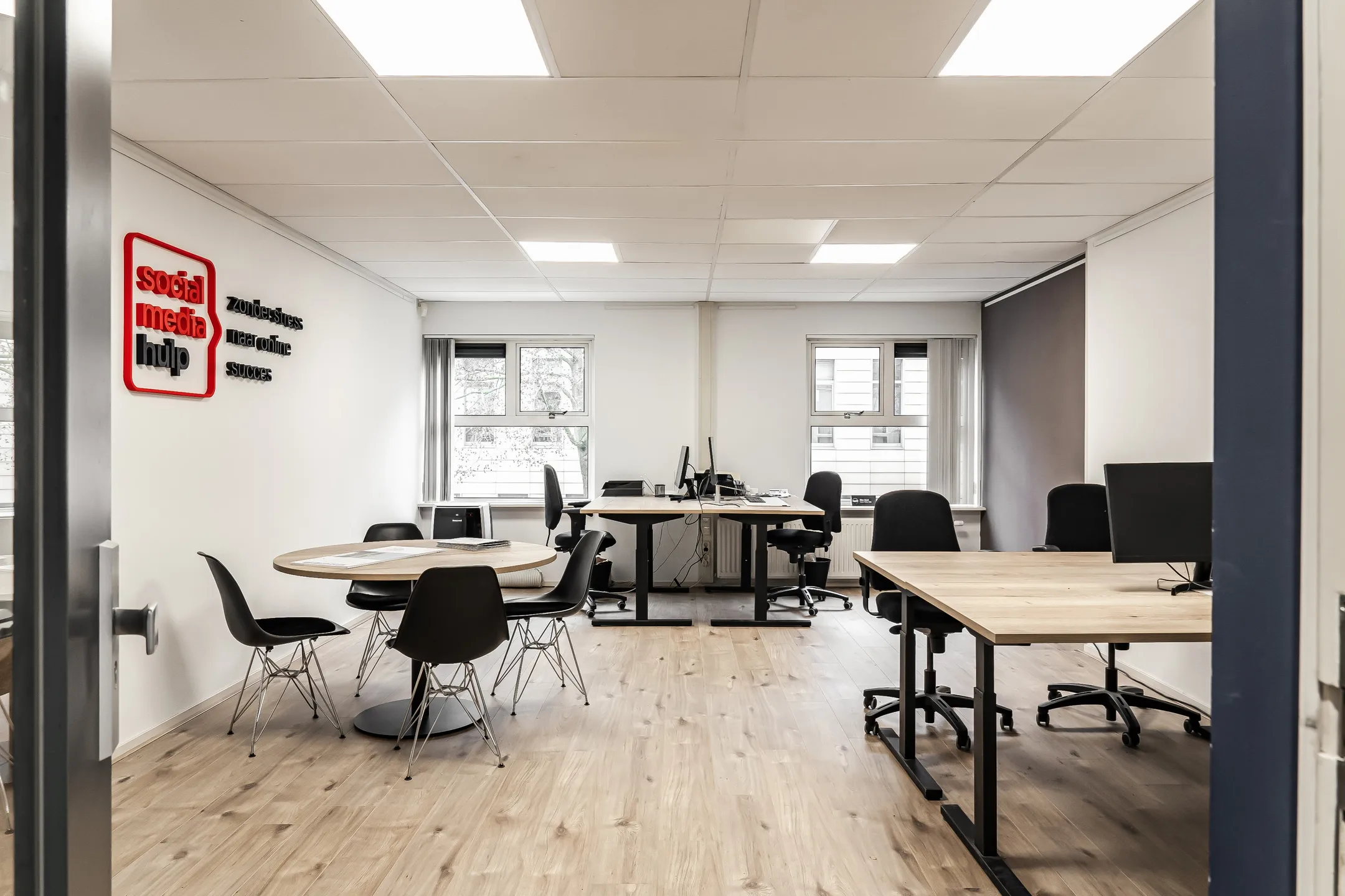 Een moderne kantoorruimte met bureaus, stoelen en een ronde tafel, met op de muur de woorden "social media hulp".