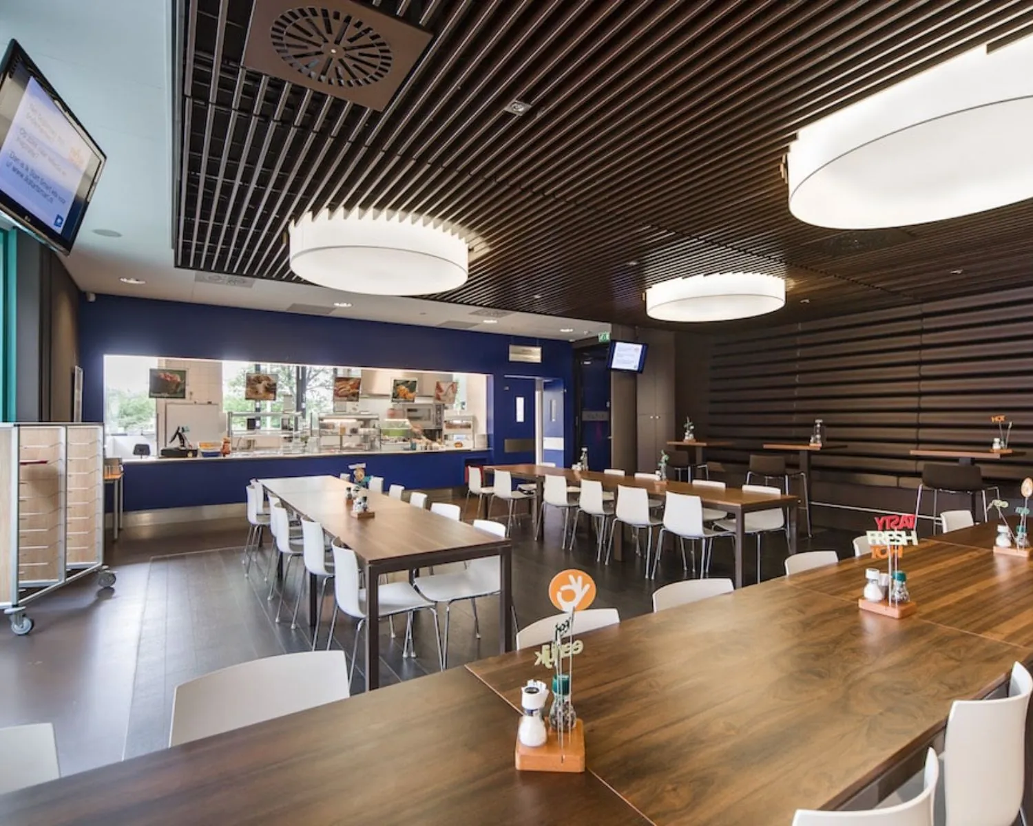 Moderne bedrijfsrestaurant met houten tafels, witte stoelen en een uitgiftebalie in een kantoorruimte aan de Kronenburgsingel 525 in Arnhem.