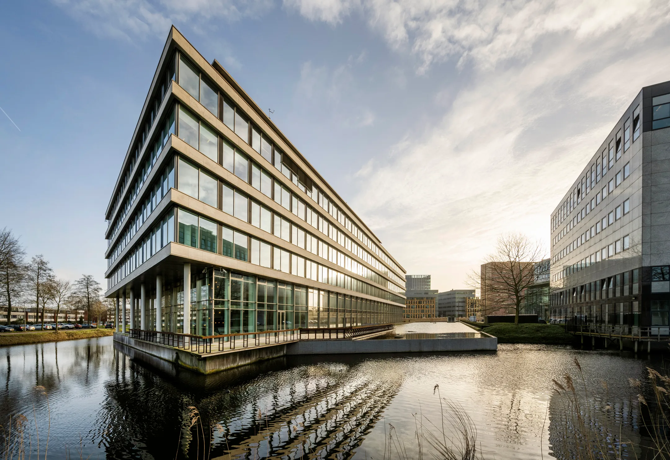 Een modern kantoorgebouw met grote ramen gelegen naast een waterpartij onder een helderblauwe lucht.
