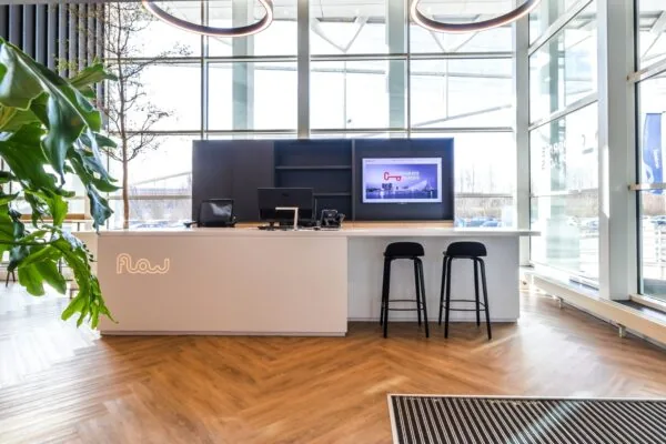 Moderne ontvangstbalie van Flow aan de Reactorweg met houten vloer, hoge ramen en een beeldscherm achter de balie.