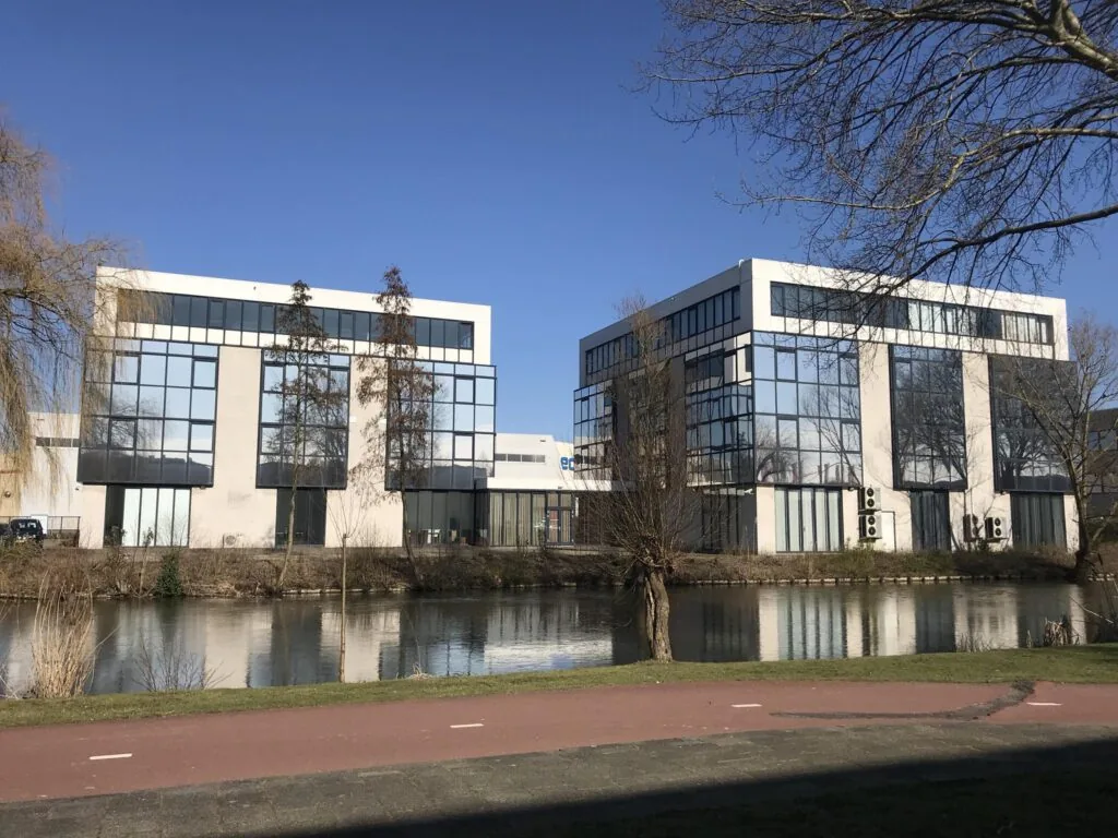 Twee moderne kantoorgebouwen aan de Cypresbaan weerspiegelen in het water van een aangrenzende sloot.