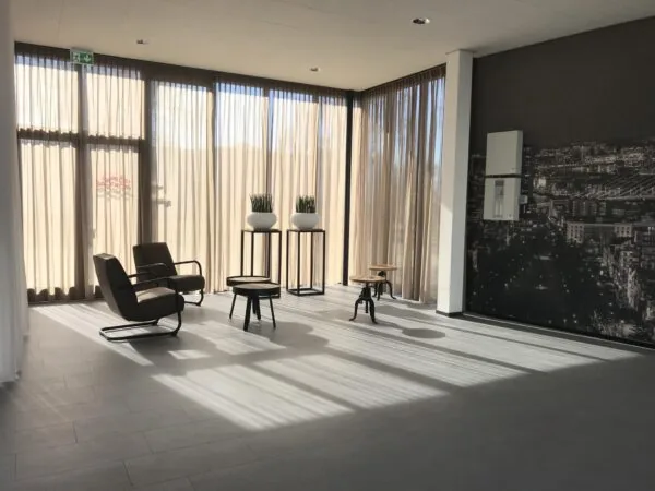 Lichte, moderne wachtruimte met stoelen, planten en een grote stadsfoto op de muur aan de Cypresbaan.