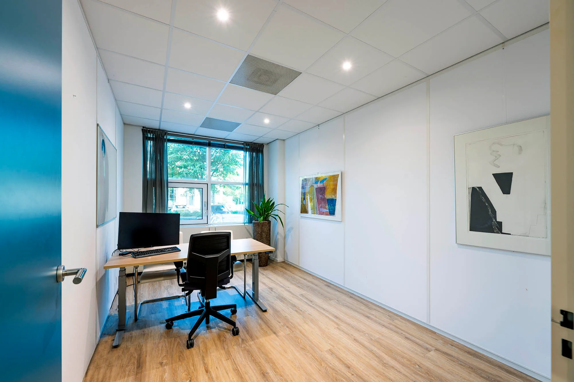 Een modern ingerichte kantoorruimte met een bureau, stoel, computer en kunst aan de muren.