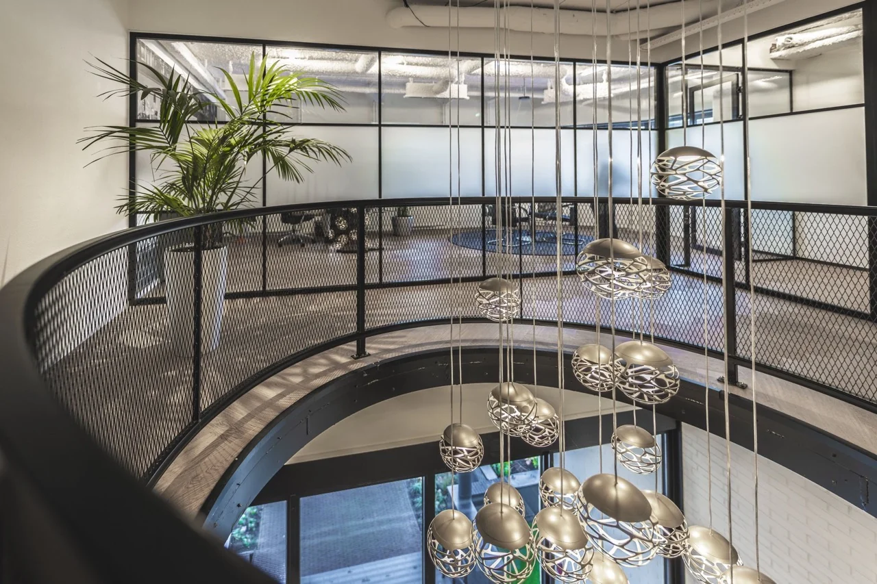 Moderne kantoorruimte met metalen balustrade, hanglampen en glazen vergaderruimtes.