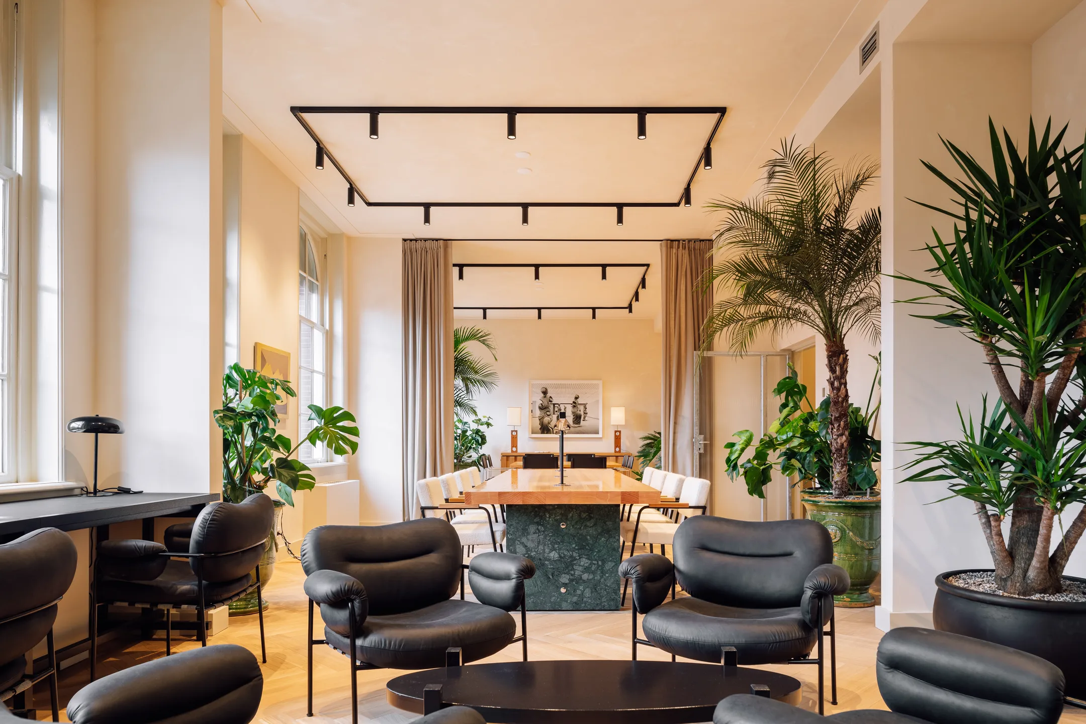Een moderne en stijlvolle woonkamer met zwarte fauteuils, veel natuurlijk licht en groene planten.
