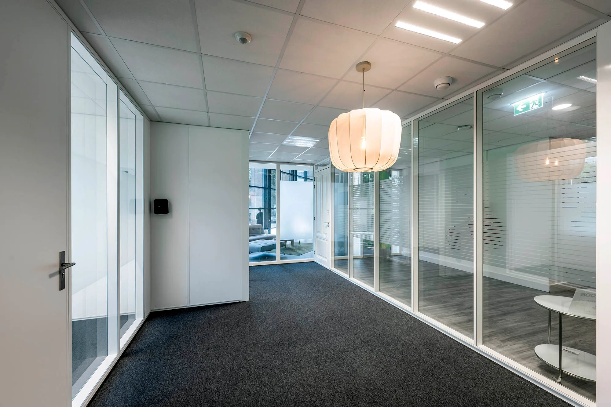 Een moderne kantoorruimte met glazen wanden en een hanglamp.