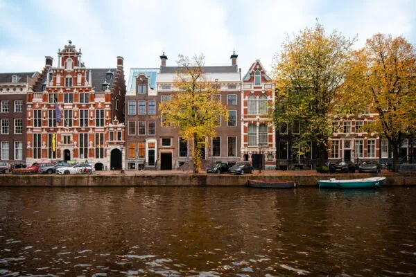 Gevels van historische panden aan een Amsterdamse gracht met herfstkleuren en boten in het water.