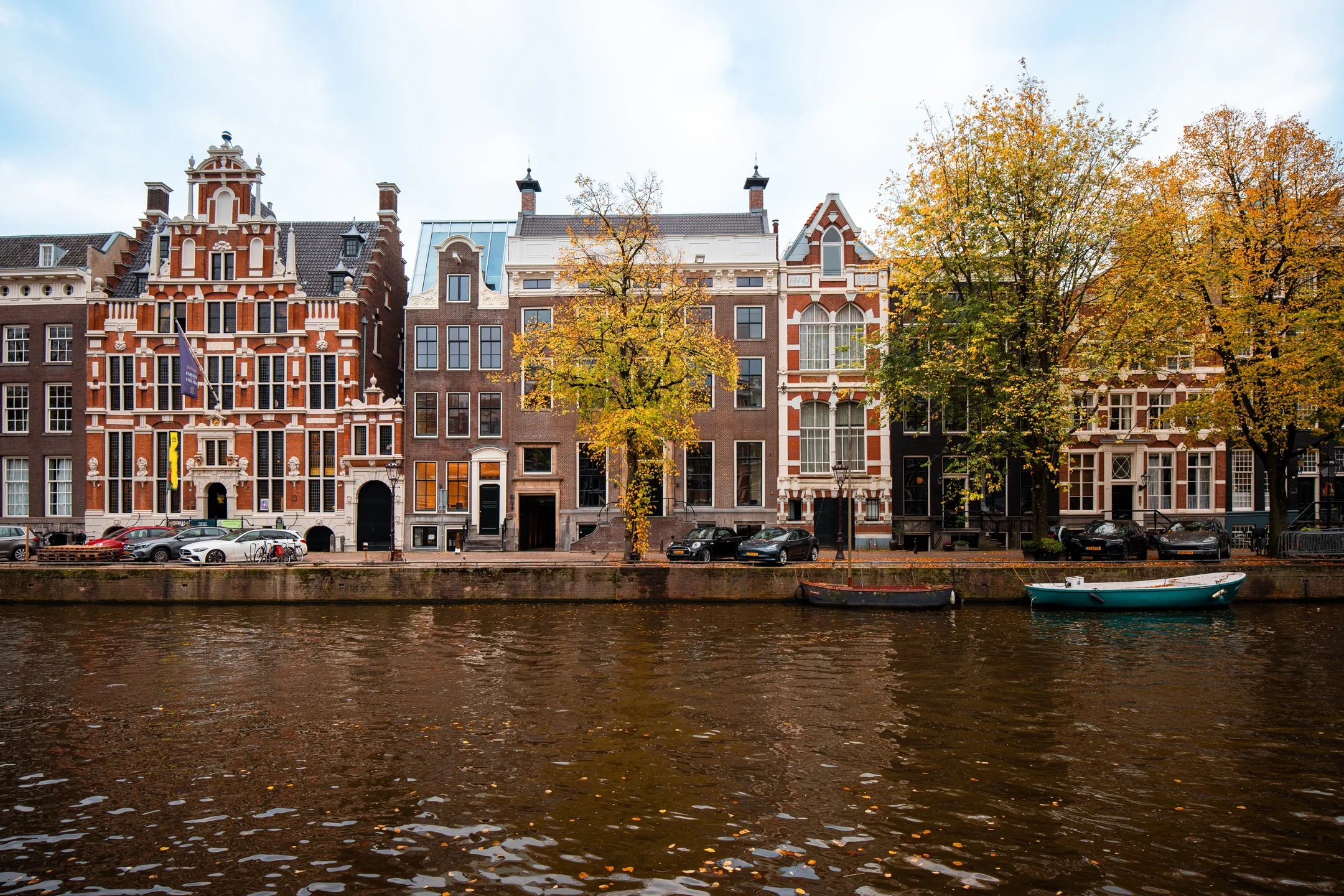 Gevels van historische panden aan een Amsterdamse gracht met herfstkleuren en boten in het water.