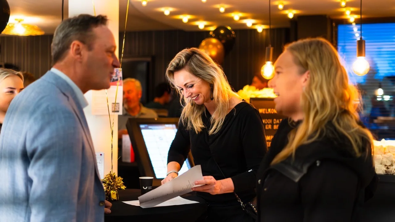 Vrolijke mensen in gesprek bij een ontvangstbalie tijdens een feestelijke gelegenheid met warme verlichting.