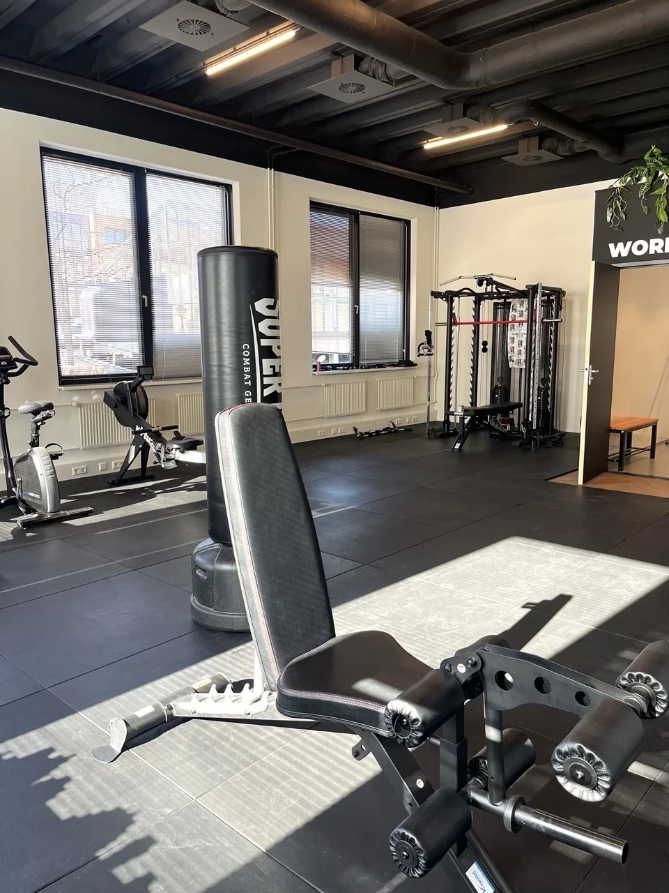 Moderne en ruime sportschool met fitnessapparatuur, een boksdummy en veel natuurlijk licht.