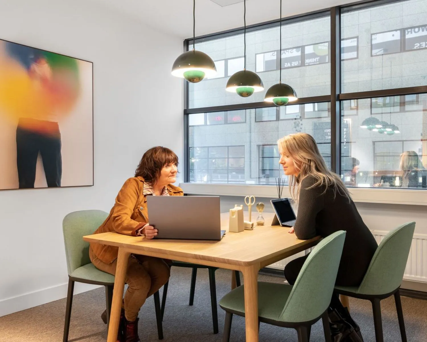 Twee vrouwen overleggen aan een houten tafel in een moderne kantoorruimte aan de Schimmelt 2-16 in Eindhoven.