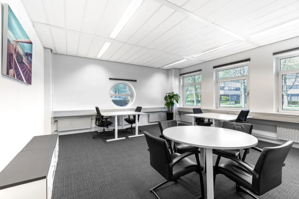 Een moderne, lichte kantoorruimte met meerdere werkplekken, bureaustoelen en een ronde vergadertafel.