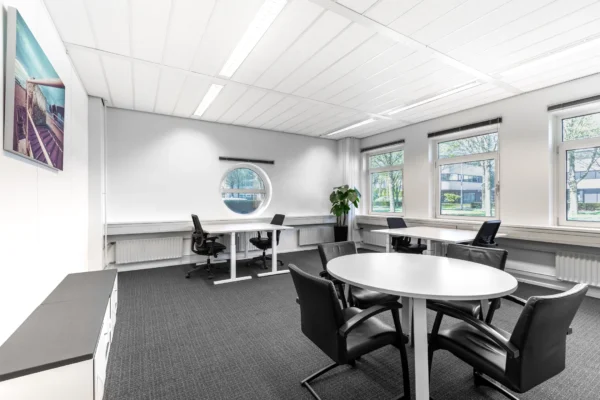 Een moderne, lichte kantoorruimte met meerdere werkplekken, bureaustoelen en een ronde vergadertafel.