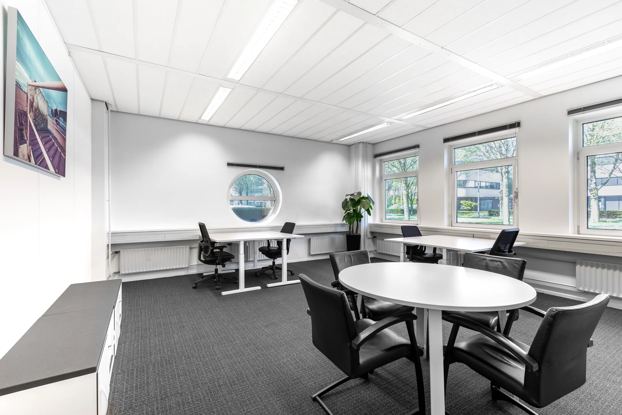 Een moderne, lichte kantoorruimte met meerdere werkplekken, bureaustoelen en een ronde vergadertafel.