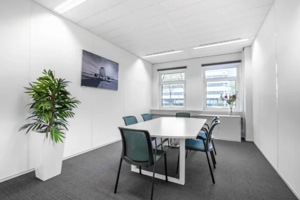 Moderne vergaderruimte met een tafel, zes stoelen, een schilderij van een vliegtuig en grote ramen.