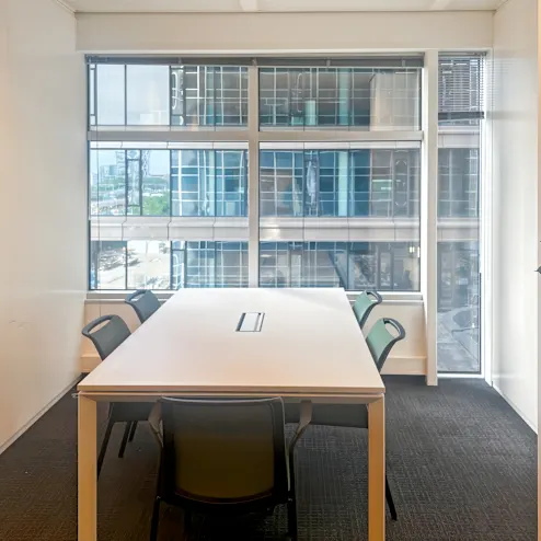 Een vergaderruimte met een tafel en stoelen voor een groot raam met uitzicht op een kantoorgebouw.