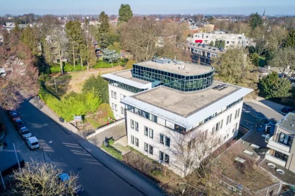 Luchtfoto van een modern kantoorgebouw aan de Amalialaan, omgeven door bomen en een woonwijk.